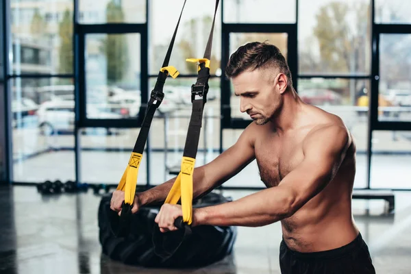 Handsome shirtless sportive man training with resistance bands in gym — Stock Photo