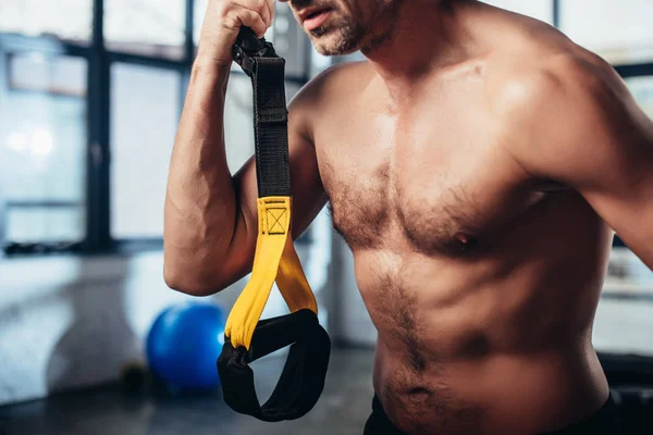 Cropped image of shirtless sportsman holding resistance bands in gym — Stock Photo