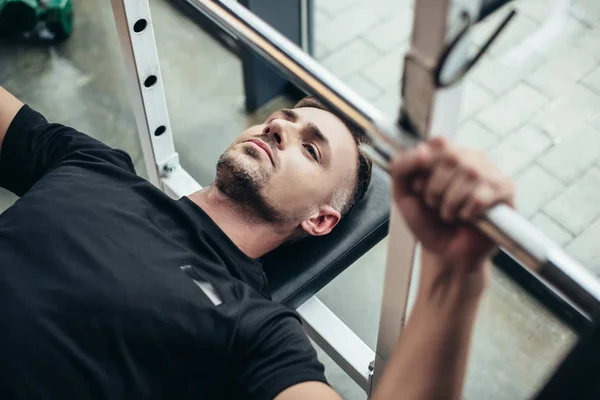 Selective focus of sportsman lifting barbell while lying on bench in gym — Stock Photo