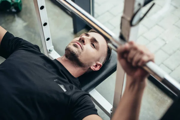 Selektiver Fokus des Sportlers beim Heben der Langhantel im Liegen auf der Bank im Fitnessstudio — Stockfoto