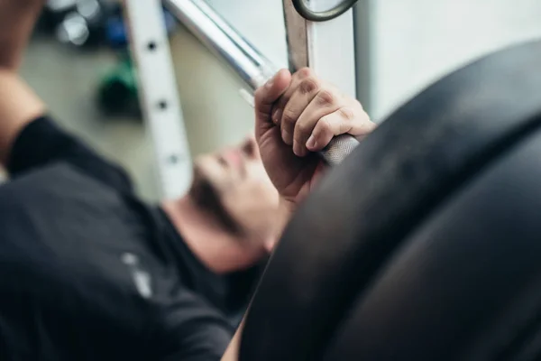 Messa a fuoco selettiva dello sportivo che solleva il bilanciere con pesi mentre è sdraiato sulla panchina in palestra — Foto stock