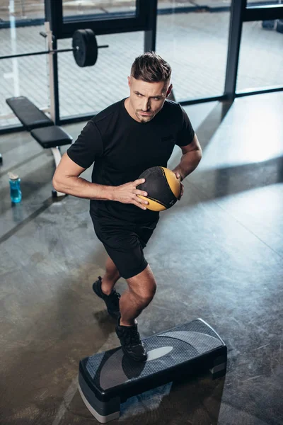 High angle view of handsome sportsman training on step platform with medicine ball in gym — Stock Photo
