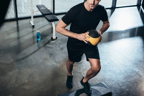 Imagen recortada del entrenamiento de deportista en la plataforma escalonada con balón de medicina en el gimnasio - foto de stock