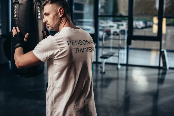 Vue arrière de l'entraîneur personnel touchant sac de boxe dans la salle de gym — Photo de stock