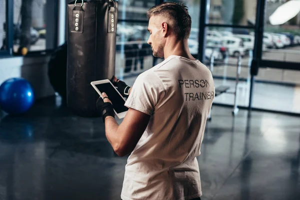Back view of personal trainer using tablet near punching bag in gym — Stock Photo