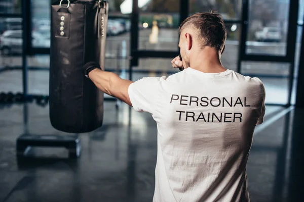 Back view of personal trainer boxing with punching bag in gym — Stock Photo