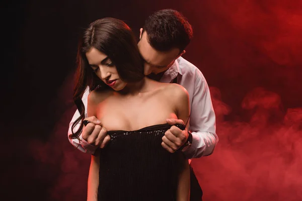Passionate man undressing his girlfriend in red smoky room — Stock Photo