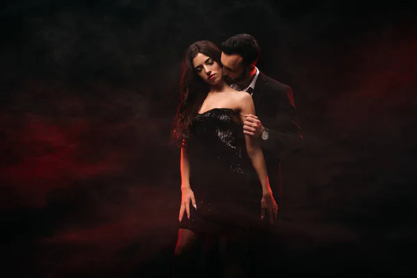 Bonito homem abraçando sedutora mulher no vermelho fumaça quarto — Fotografia de Stock