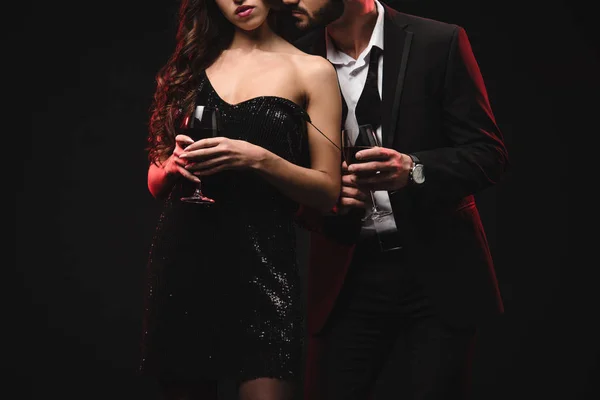 Vista recortada de pareja seductora sosteniendo vasos con vino tinto aislado en negro - foto de stock