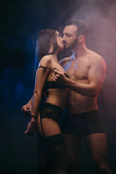 Sinnliches Paar mit Handschellen küsst sich im verrauchten Zimmer — Stockfoto