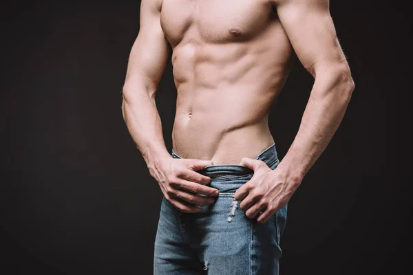 Обрезанный вид сексуального мужчины без рубашки в джинсах, изолированных на черном — стоковое фото