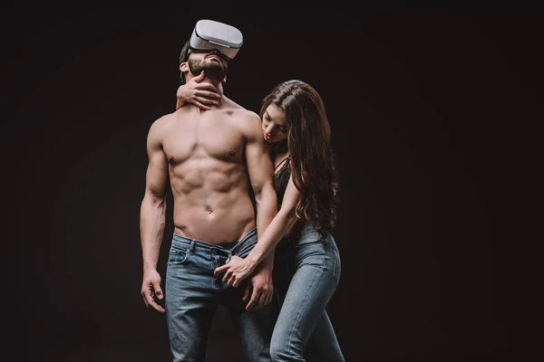 Beautiful girl undressing shirtless man in vr headset isolated on black — Stock Photo