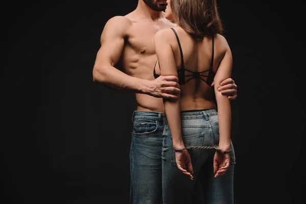 Cropped view of shirtless man hugging passionate girlfriend in handcuffs isolated on black — Stock Photo