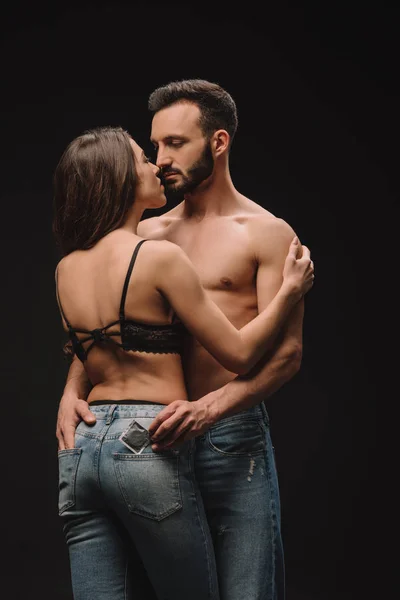 Guapo sin camisa hombre abrazando novia y sosteniendo condón aislado en negro - foto de stock