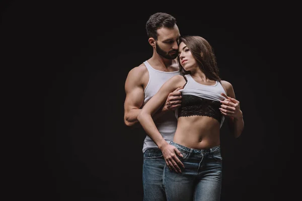 Hombre guapo desnudando chica en sujetador de encaje aislado en negro - foto de stock