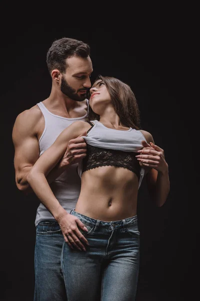 Sexual man undressing girl in singlet isolated on black — Stock Photo