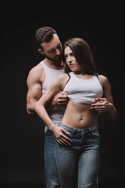 Handsome boyfriend hugging girl in white singlet isolated on black — Stock Photo