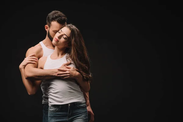 Bell'uomo che abbraccia e bacia giovane donna isolata su nero — Foto stock