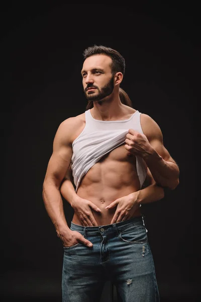 Young woman hugging and undressing sexy man isolated on black — Stock Photo