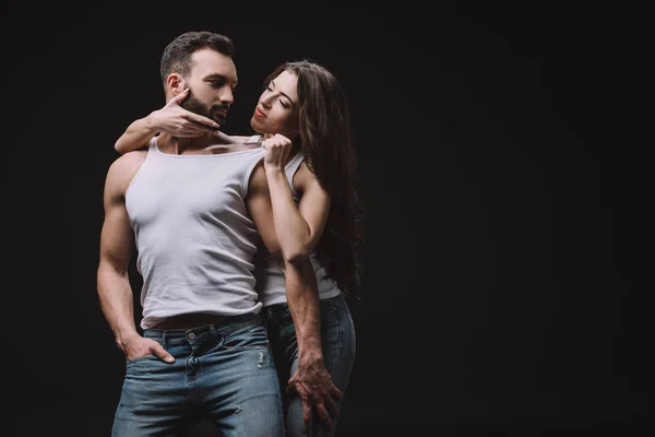 Sexy woman hugging and undressing man in white singlet isolated on black — Stock Photo