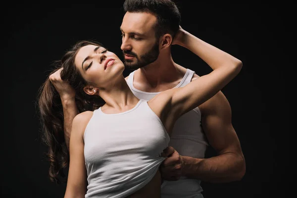 Sexy hombre abrazando y desvestirse chica en blanco singlet aislado en negro - foto de stock