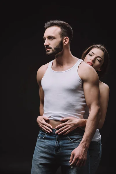 Sexual girl hugging boyfriend in white singlet isolated on black — Stock Photo