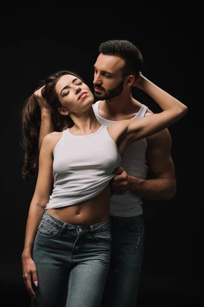 Passionate man undressing girl in white singlet isolated on black — Stock Photo