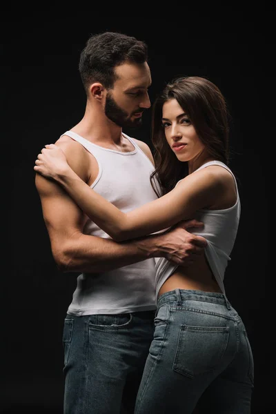 Man hugging and undressing girl in white singlet isolated on black — Stock Photo
