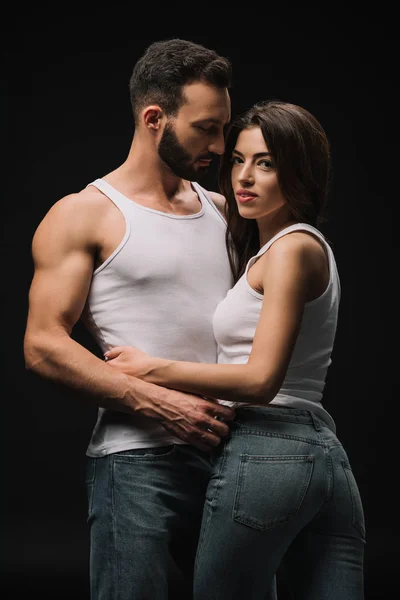 Guapo hombre abrazando chica en blanco singlet aislado en negro - foto de stock