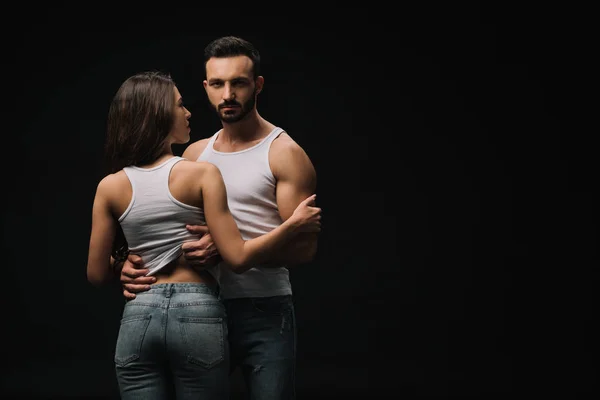 Sexual couple in white singlets and jeans isolated on black — Stock Photo