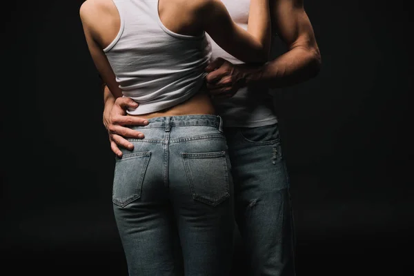 Vista recortada de pareja en singlets blancos y jeans aislados en negro - foto de stock