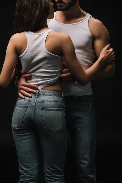 Vista cortada de casal apaixonado em singlets brancos e jeans isolados em preto — Fotografia de Stock