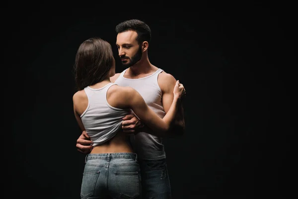 Couple passionné en singlets blancs et jeans isolés sur noir — Photo de stock