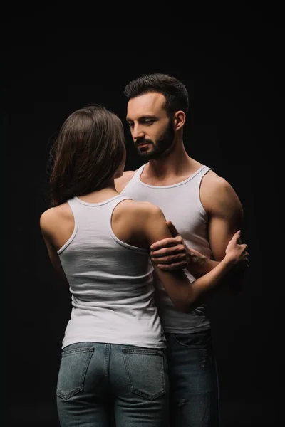 Guapo hombre abrazando chica en blanco singlet aislado en negro - foto de stock