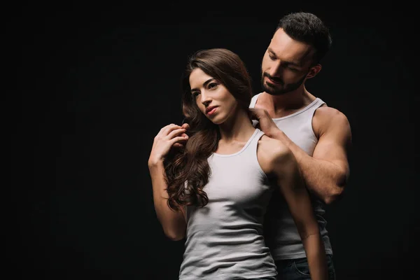 Handsome man hugging beautiful girl in white singlet isolated on black — Stock Photo