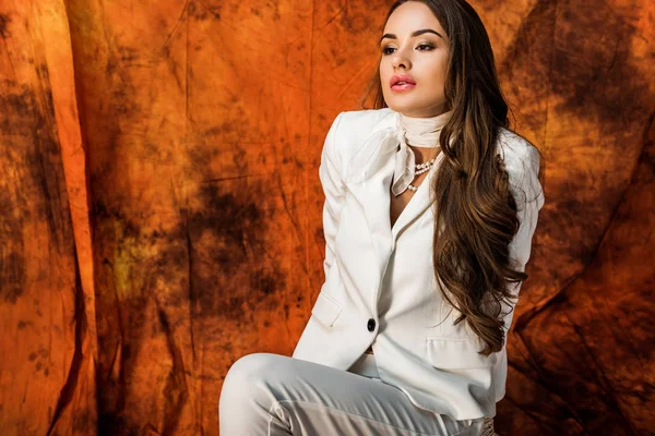 Attractive girl with long brown hair in white suit posing on chair on textured background — Stock Photo