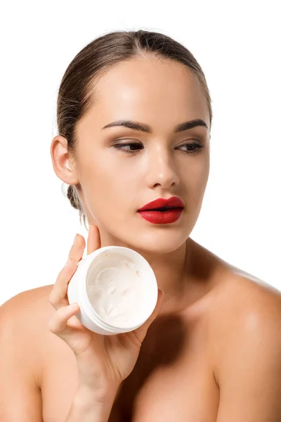 Atractiva chica con labios rojos sosteniendo tarro con crema facial aislado en blanco - foto de stock