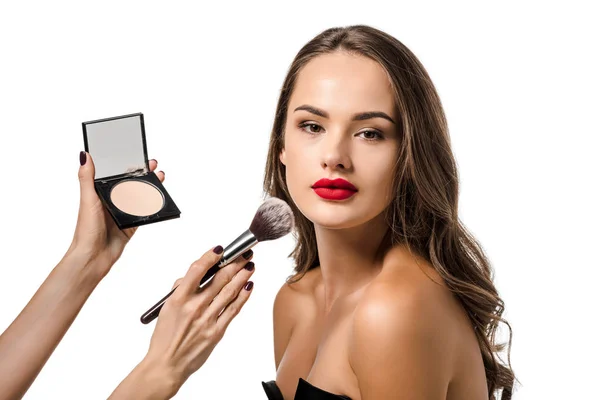 Visão recortada da mulher aplicando pó com escova cosmética no rosto do belo modelo olhando para a câmera isolada no branco — Fotografia de Stock