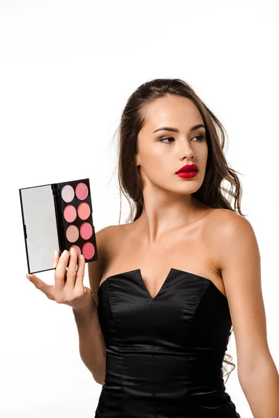 Atractiva chica en vestido negro con labios rojos sosteniendo paleta con sombras de ojos aislados en blanco - foto de stock