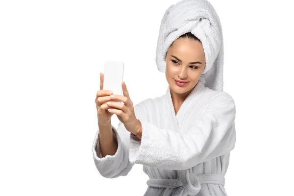 Jolie fille en peignoir avec serviette sur la tête prenant selfie isolé sur blanc — Photo de stock