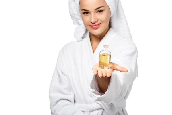 Chica atractiva en albornoz mostrando botella de aceite y mirando a la cámara aislada en blanco - foto de stock