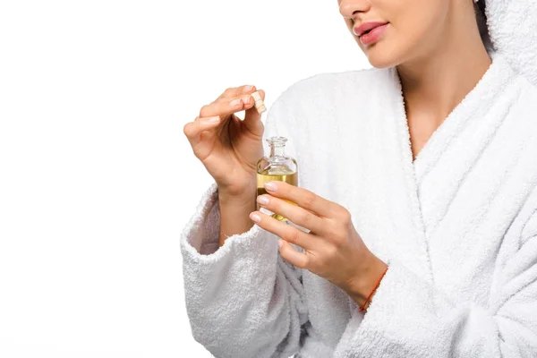 Cropped view of girl in bathrobe holding opened bottle of oil isolated on white — Stock Photo