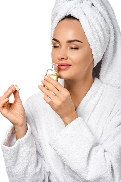 Attractive girl in bathrobe sniffing opened bottle of oil isolated on white — Stock Photo
