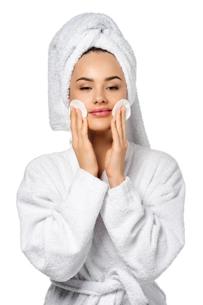 Attractive girl in bathrobe cleaning face with cotton sponges and looking at camera isolated on white — Stock Photo