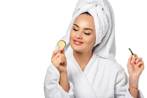 Beautiful girl in bathrobe looking at cucumber slice and smiling isolated on white — Stock Photo