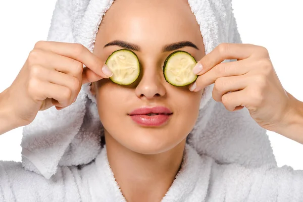 Attraktives Mädchen im Bademantel mit Gurkenscheiben in der Nähe von Augen isoliert auf weiß — Stockfoto