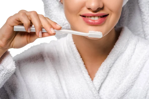 Vista recortada de chica en albornoz sosteniendo cepillo de dientes y sonriendo aislado en blanco - foto de stock