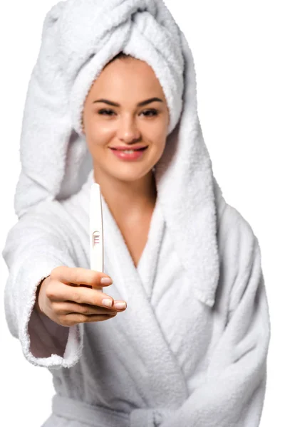 Красива дівчина в халаті з рушником на голові посміхається, показуючи тест на вагітність і дивлячись на камеру ізольовано на білому — стокове фото
