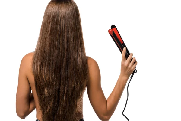 Вид сзади девушки с длинными каштановыми волосами, держащей выпрямитель волос изолированной на белом — стоковое фото