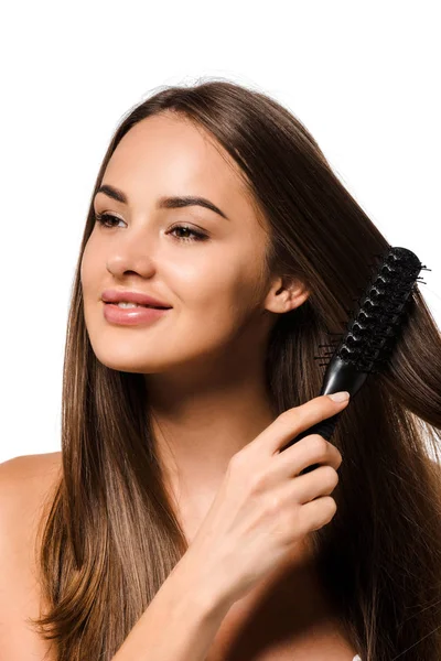 Hermosa chica peinando el cabello con cepillo de pelo y sonriendo aislado en blanco - foto de stock